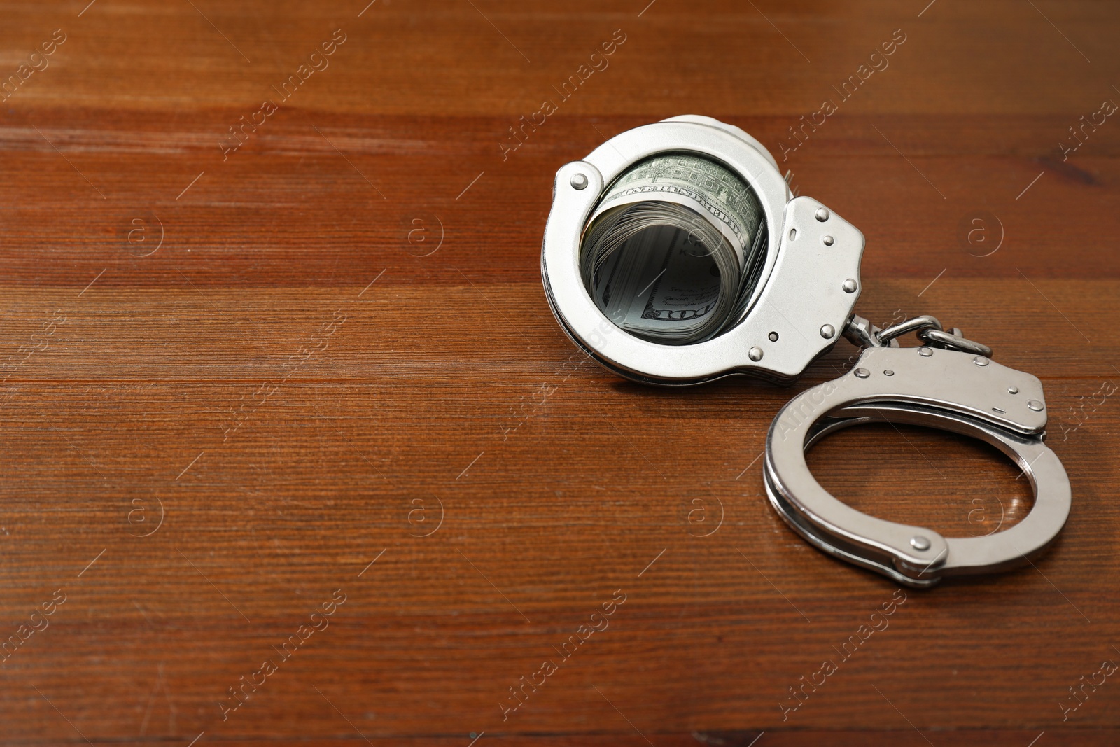 Photo of Handcuffs with dollar banknotes on wooden table, space for text