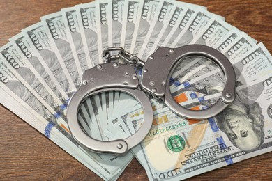 Photo of Handcuffs with dollar banknotes on wooden table