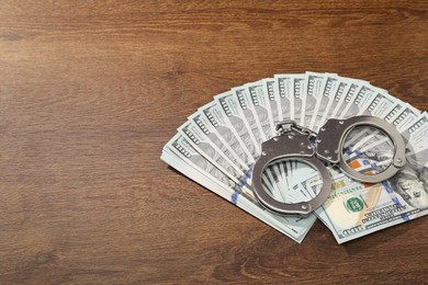 Handcuffs with dollar banknotes on wooden table, space for text