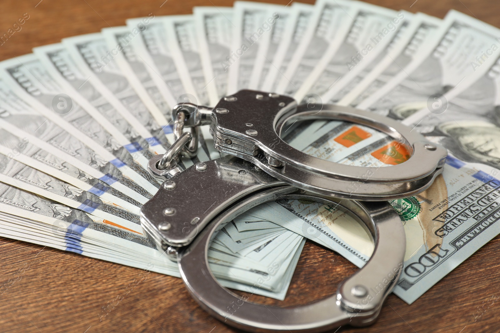 Photo of Handcuffs with dollar banknotes on wooden table, closeup