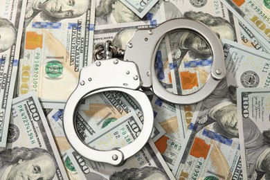 Photo of Handcuffs on pile of dollar banknotes, flat lay