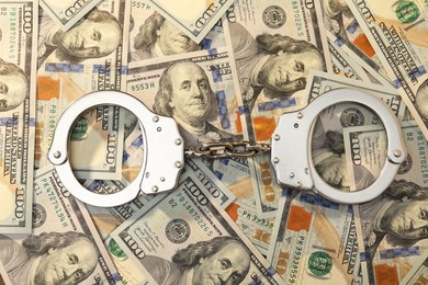 Handcuffs on pile of dollar banknotes, flat lay