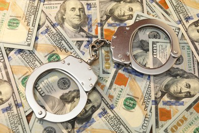 Handcuffs on pile of dollar banknotes, above view