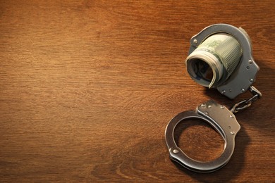 Handcuffs with dollar banknotes on wooden table, space for text