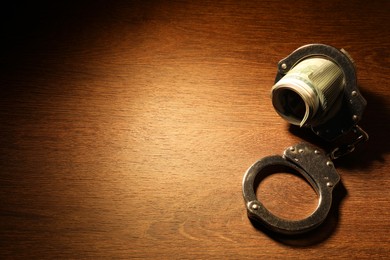 Handcuffs with dollar banknotes on wooden table, space for text