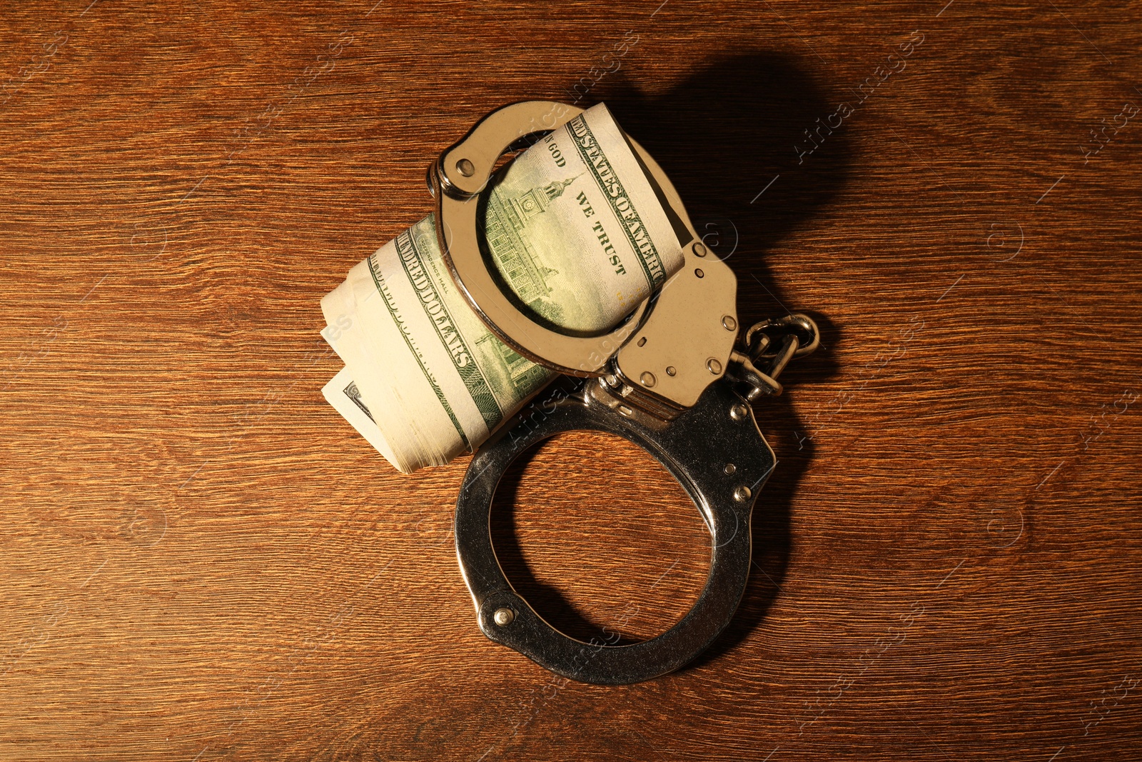 Photo of Handcuffs with dollar banknotes on wooden table, top view