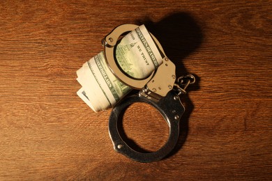 Handcuffs with dollar banknotes on wooden table, top view