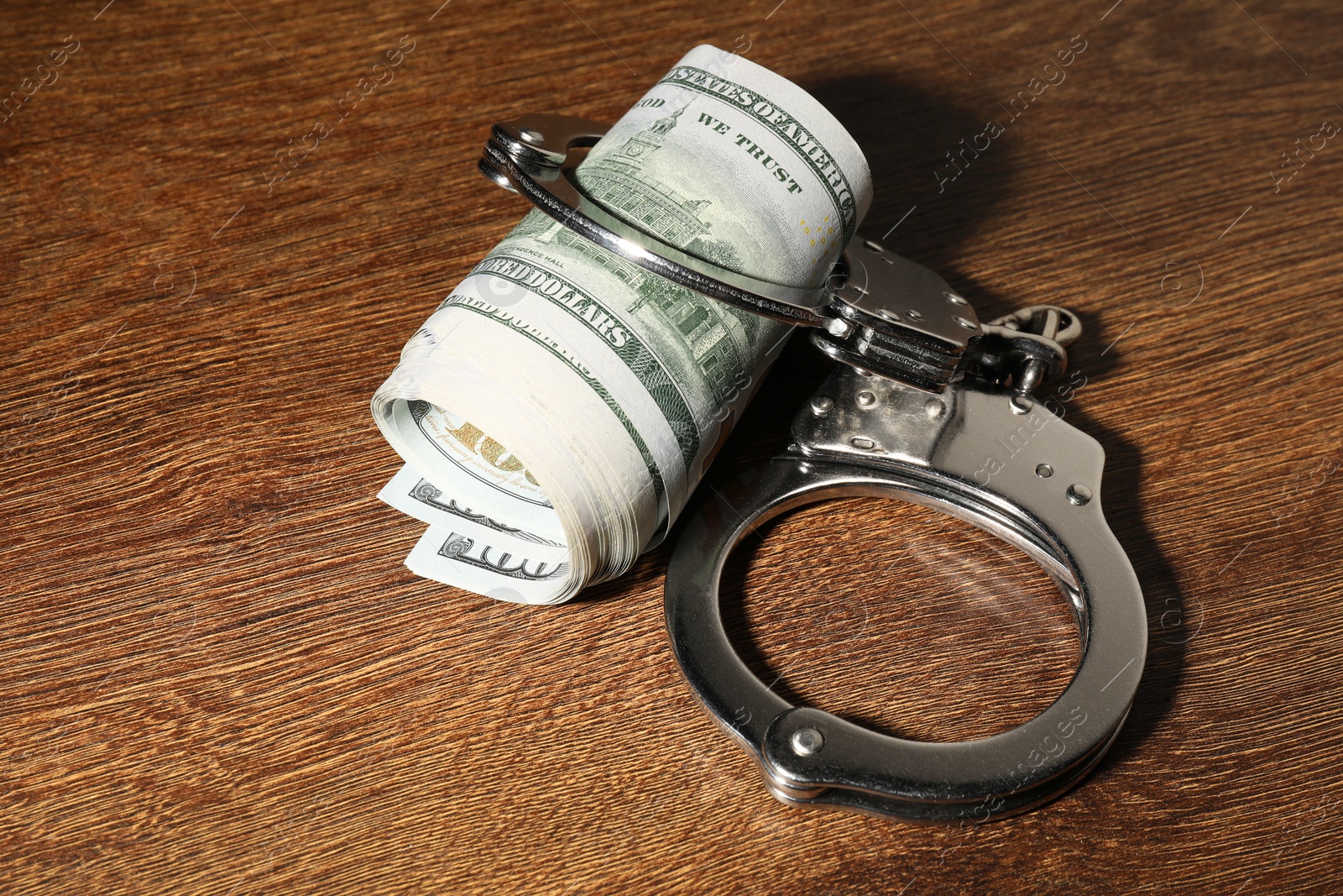 Photo of Handcuffs with dollar banknotes on wooden table