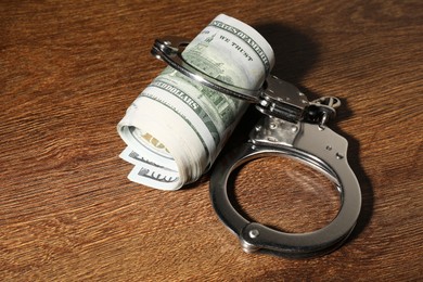 Handcuffs with dollar banknotes on wooden table