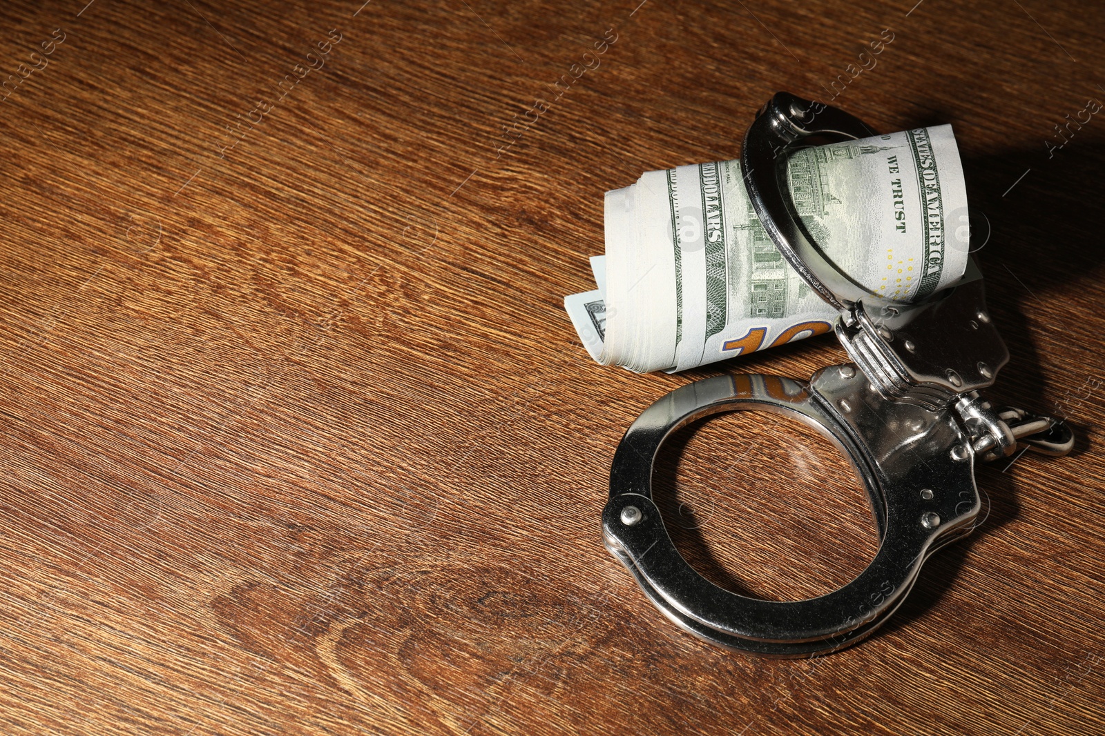 Photo of Handcuffs with dollar banknotes on wooden table, space for text