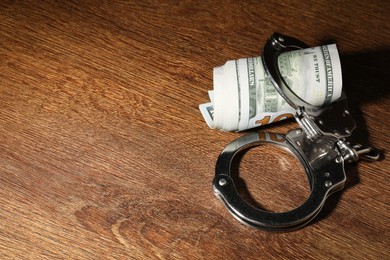 Handcuffs with dollar banknotes on wooden table, space for text