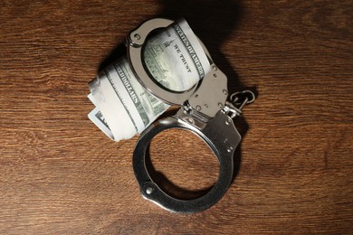 Photo of Handcuffs with dollar banknotes on wooden table, top view