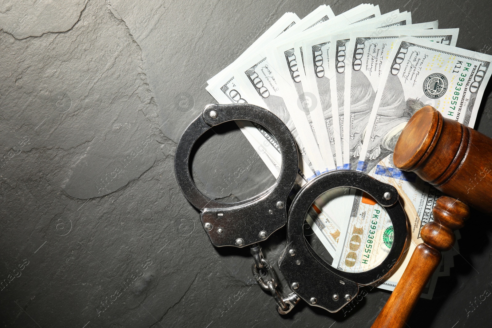 Photo of Handcuffs with dollar banknotes and wooden gavel on grey textured table, flat lay. Space for text