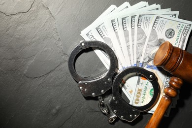 Handcuffs with dollar banknotes and wooden gavel on grey textured table, flat lay. Space for text