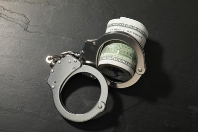 Handcuffs with dollar banknotes on grey textured table