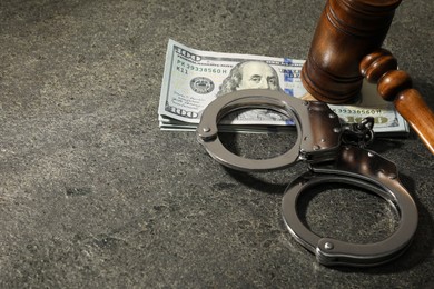 Handcuffs with dollar banknotes and wooden gavel on grey textured table, space for text