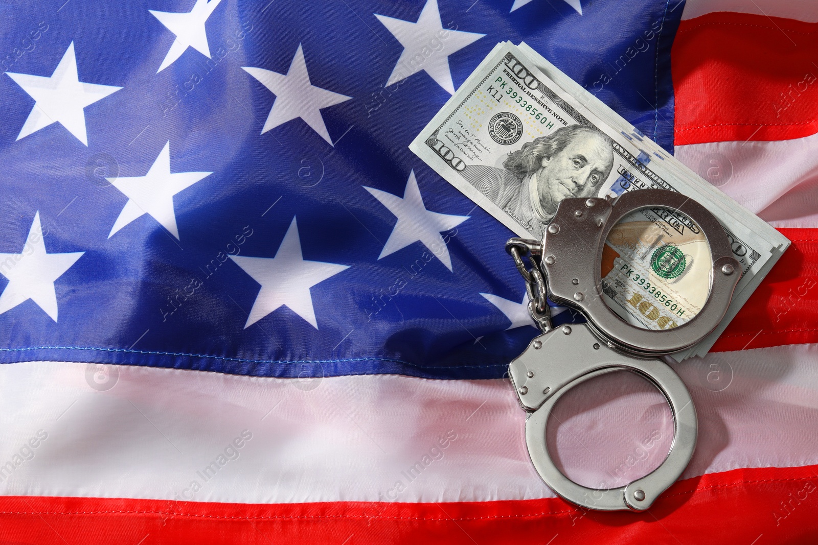 Photo of Handcuffs with dollar banknotes on American flag, flat lay. Space for text