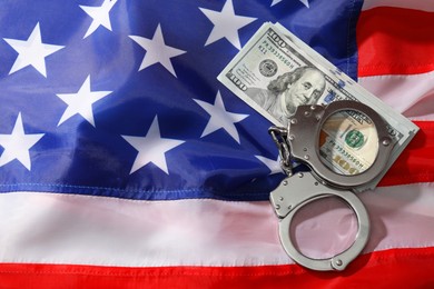 Handcuffs with dollar banknotes on American flag, flat lay. Space for text