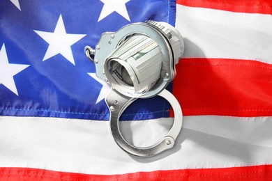 Photo of Handcuffs with dollar banknotes on American flag, top view