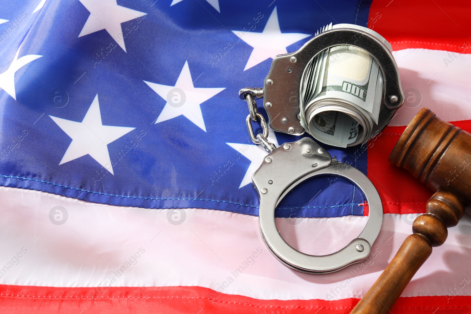 Photo of Handcuffs with dollar banknotes and wooden gavel on American flag, space for text