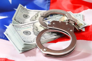 Handcuffs with dollar banknotes on American flag, closeup