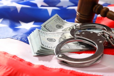 Photo of Handcuffs with dollar banknotes and wooden gavel on American flag