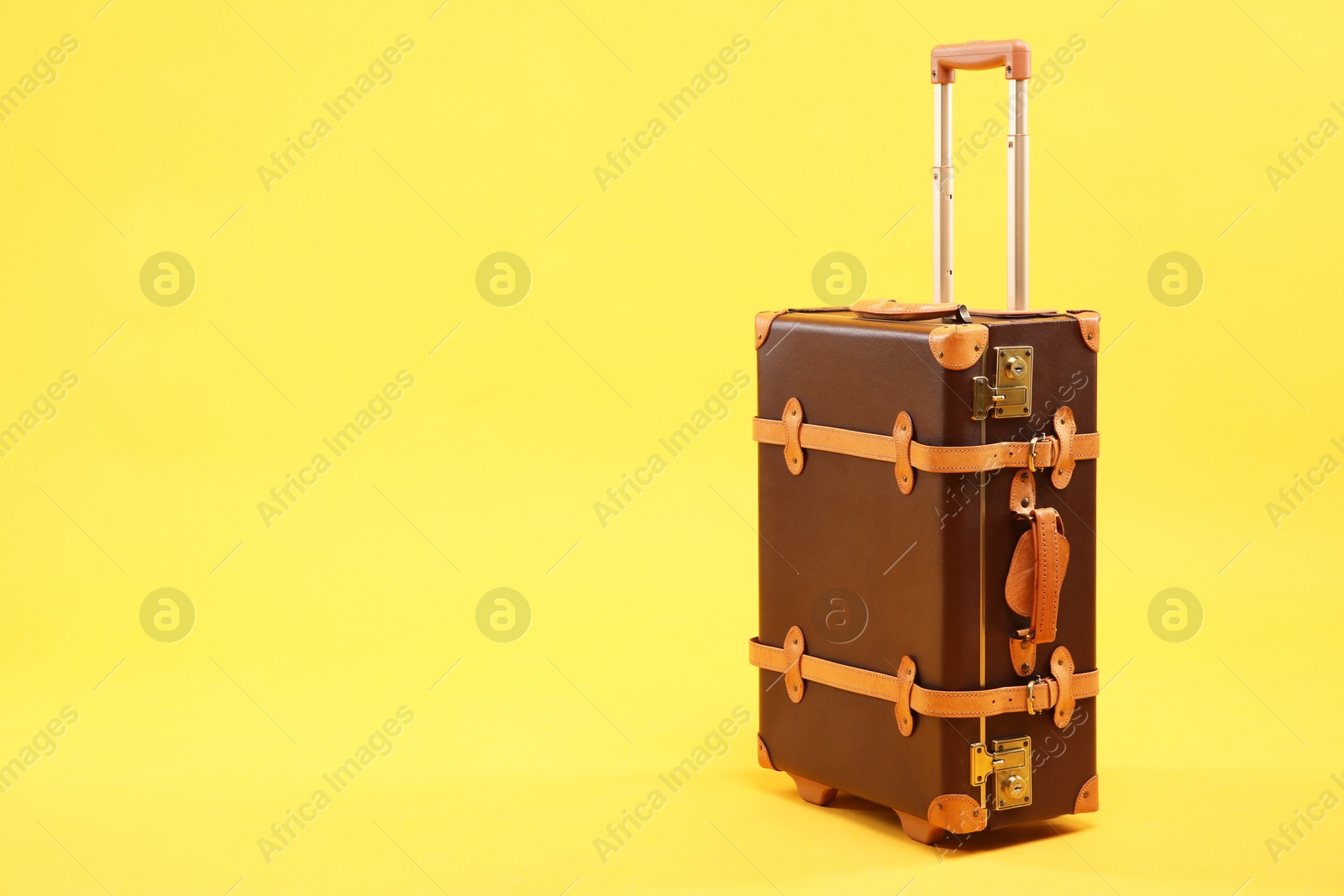 Photo of One new brown suitcase on yellow background, space for text