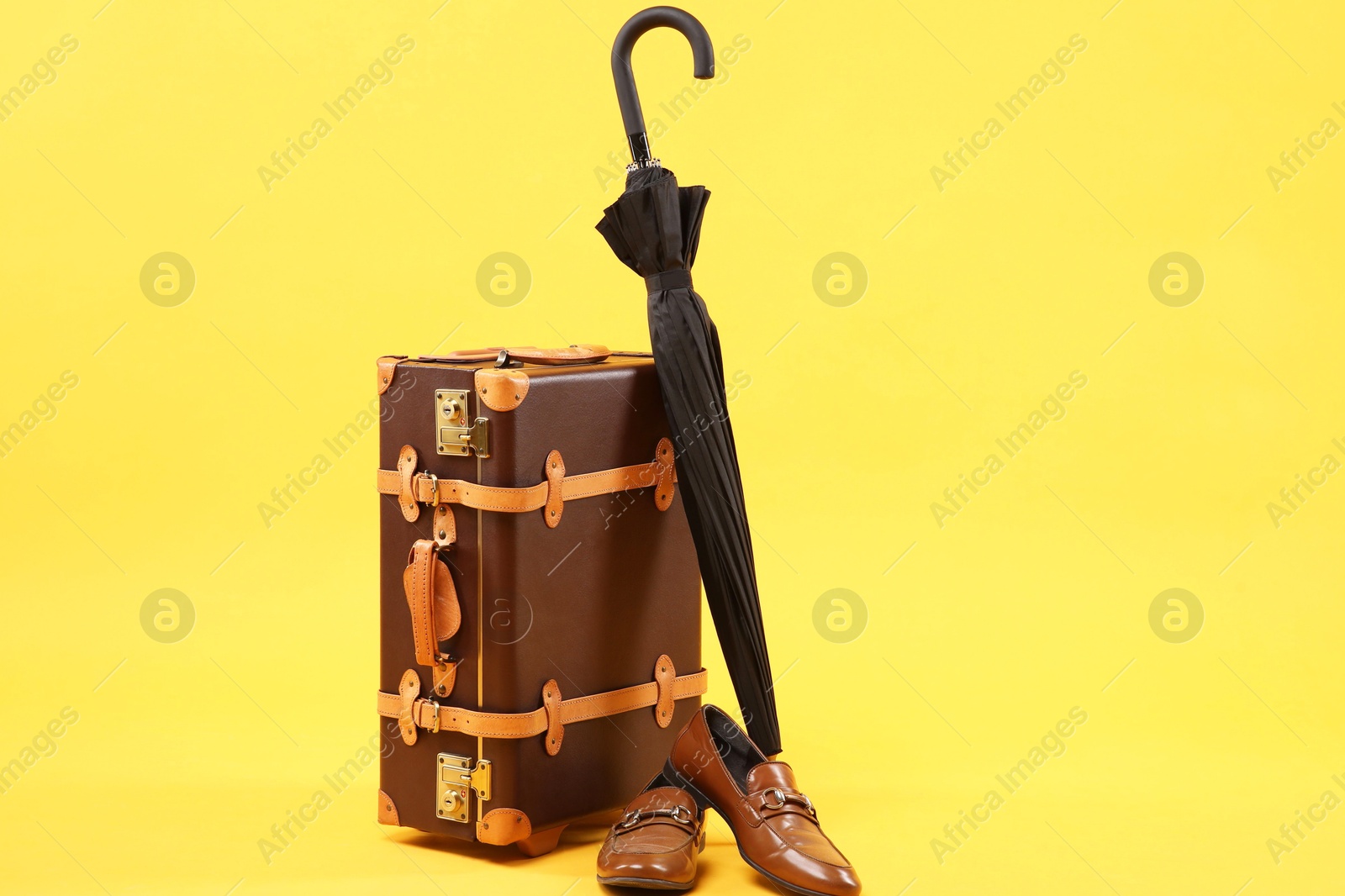 Photo of Brown suitcase, shoes and umbrella on yellow background, space for text