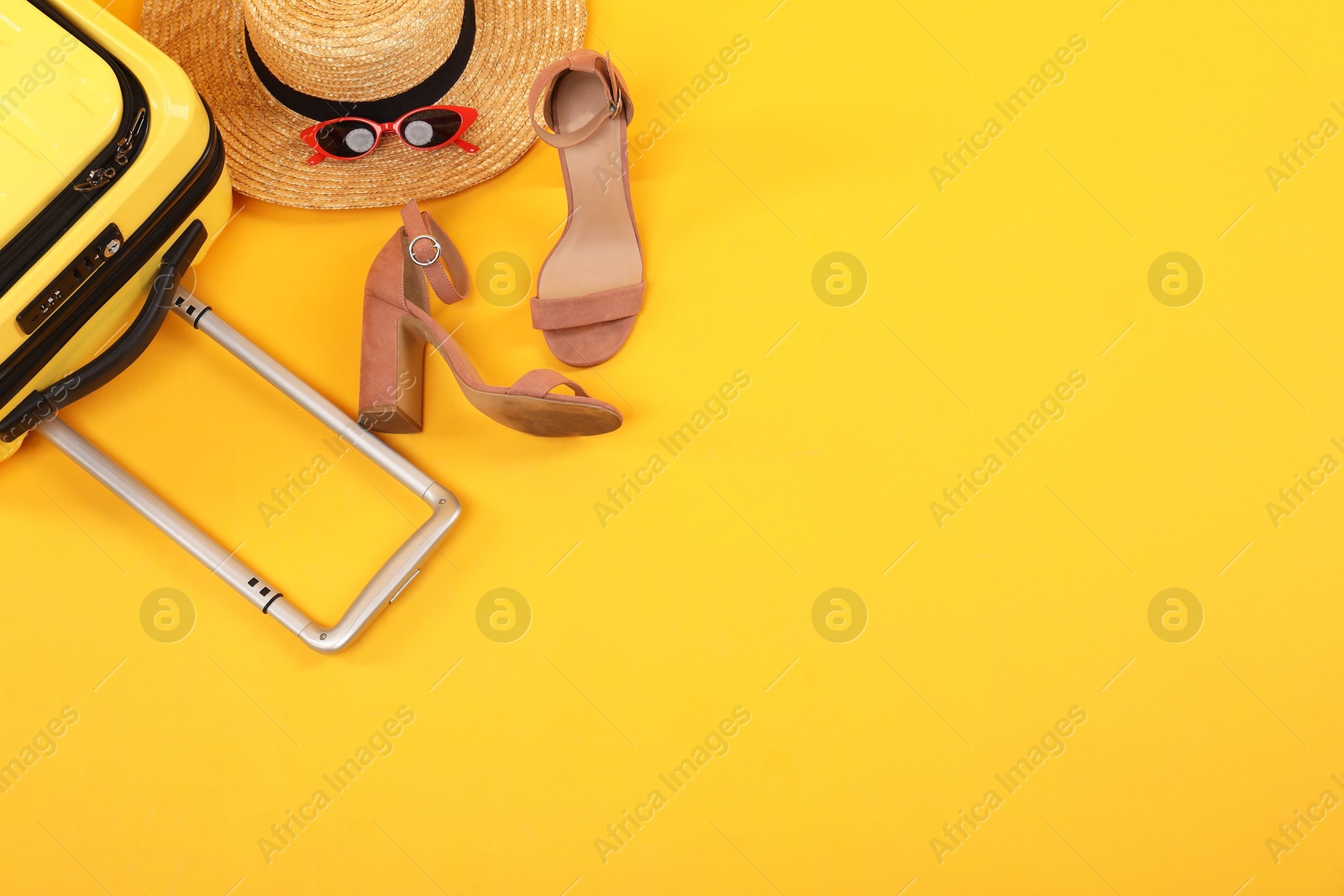 Photo of Suitcase with wicker hat, sunglasses and shoes on yellow background, flat lay. Space for text