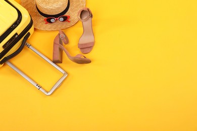 Suitcase with wicker hat, sunglasses and shoes on yellow background, flat lay. Space for text