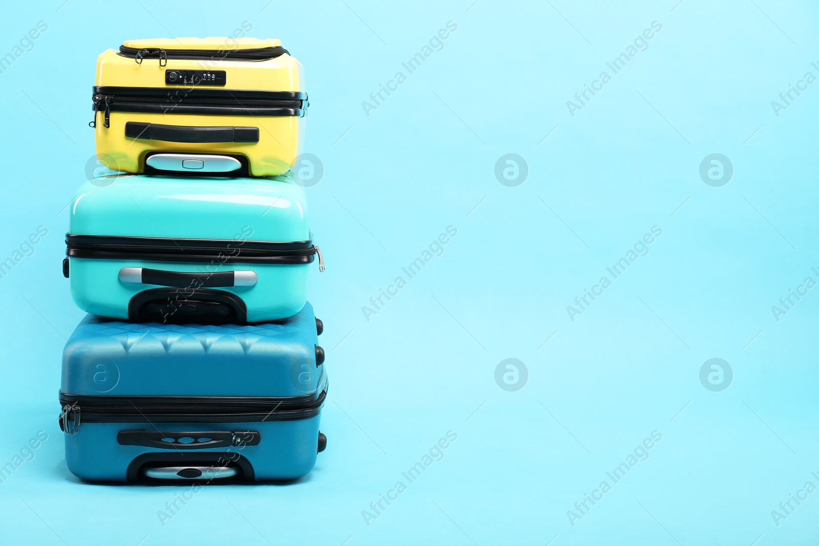 Photo of Stack of different suitcases on light blue background, space for text