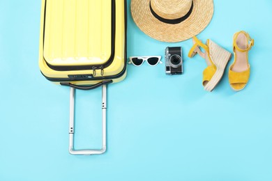 Yellow suitcase, shoes, sunglasses, wicker hat and camera on light blue background, flat lay