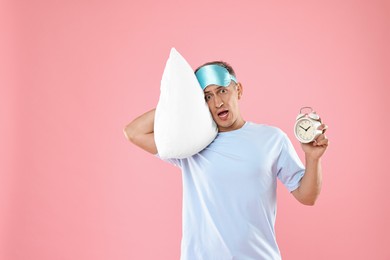 Photo of Overslept man with sleep mask, pillow and alarm clock on pink background, space for text