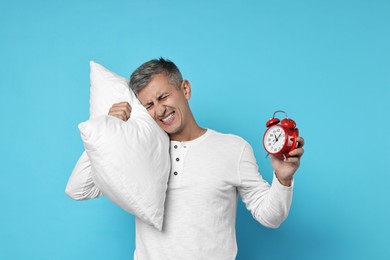 Photo of Overslept man with pillow and alarm clock on light blue background