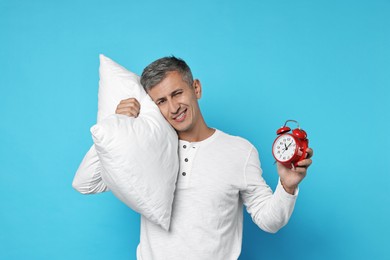 Overslept man with pillow and alarm clock on light blue background