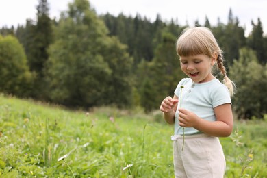 Happy little girl with flower at meadow, space for text. Child enjoying beautiful nature