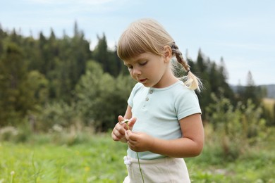 Cute little girl with flower at meadow, space for text. Child enjoying beautiful nature