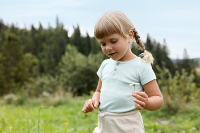 Cute little girl with flower at meadow, space for text. Child enjoying beautiful nature