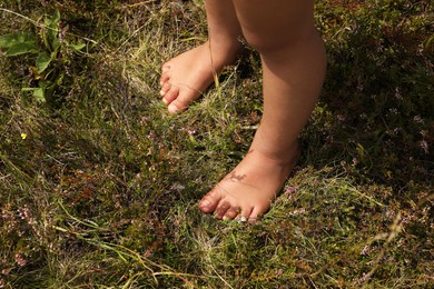 Photo of Little girl standing barefoot outdoors on sunny day, closeup. Child enjoying beautiful nature