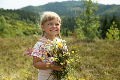 Photo of Smiling little girl with bouquet of wildflowers at field. Child enjoying beautiful nature