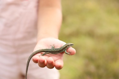 Little girl holding lizard on blurred background, closeup, space for text. Child enjoying beautiful nature