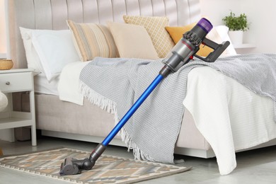 Photo of One cordless vacuum cleaner leaning on bed indoors