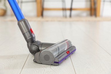 Photo of Cleaning floor with cordless vacuum cleaner indoors, closeup. Space for text