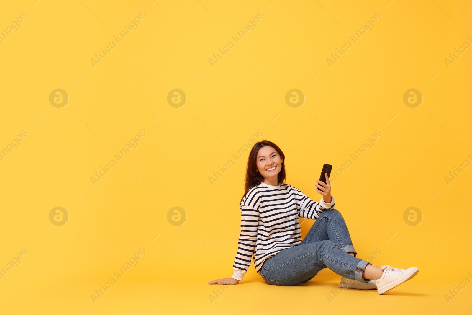 Photo of Smiling young woman with smartphone on yellow background. Space for text