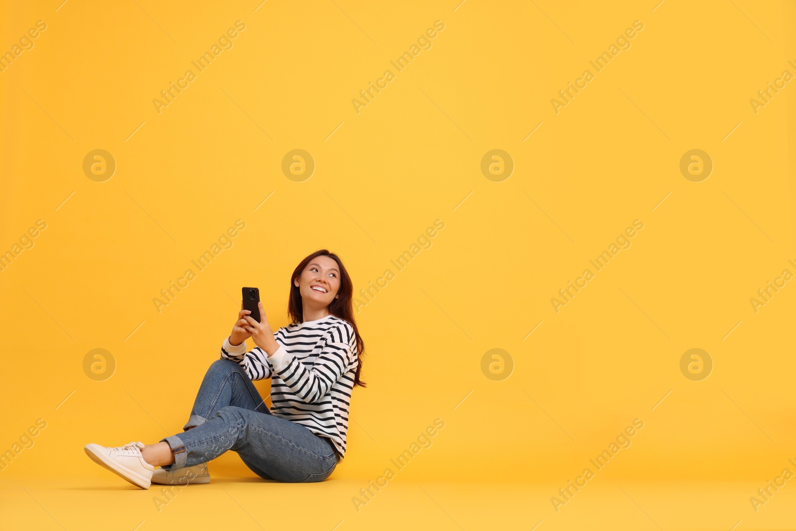 Photo of Smiling young woman with smartphone on yellow background. Space for text