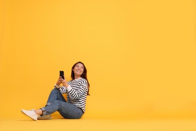 Smiling young woman with smartphone on yellow background. Space for text