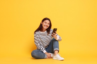 Photo of Smiling young woman using smartphone on yellow background