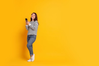 Smiling young woman with smartphone on yellow background. Space for text