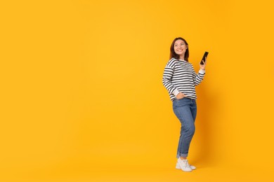 Photo of Smiling young woman with smartphone on yellow background. Space for text