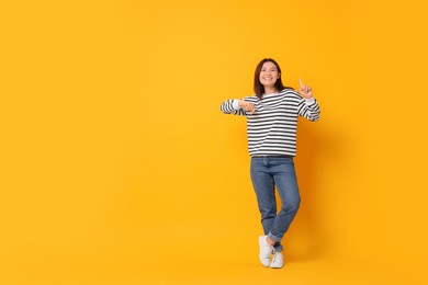 Photo of Smiling woman pointing at something on yellow background. Space for text